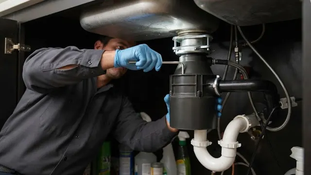 A plumber installing a garbage disposal under a kitchen sink